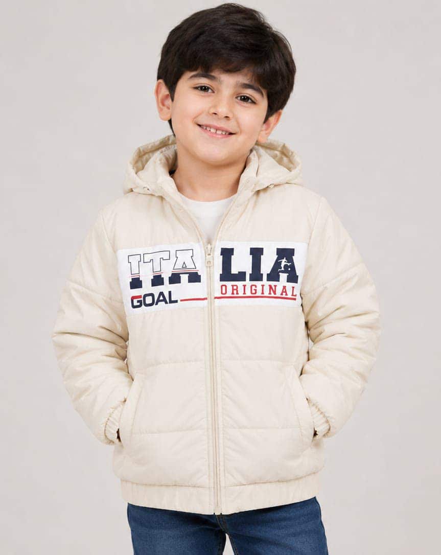 A boy in a cream hooded puffer jacket with a printed chest panel