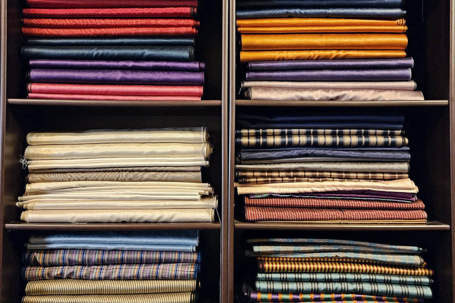 Folded cloth stacked in deep rows on shelving that runs the height of the wall